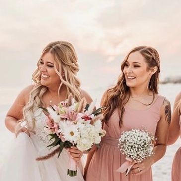 Bride and bridesmaid smiling with bouquets.