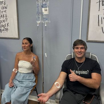 Two people donating blood, smiling and connected to IV bags.