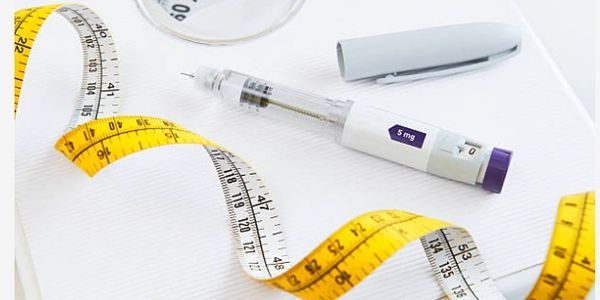 Insulin pen and measuring tape on a white surface.