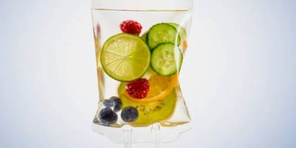A clear glass filled with water and colorful fruit slices and berries.