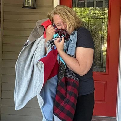Woman hugging a pile of clothes, smiling happily by a red door.