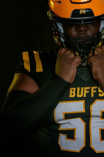 Football player in black and yellow uniform adjusting helmet.