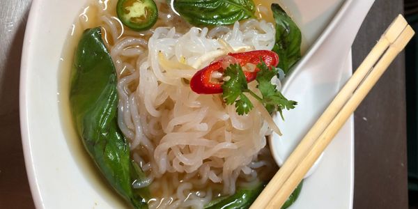 Bowl of noodle soup with herbs and chili peppers.