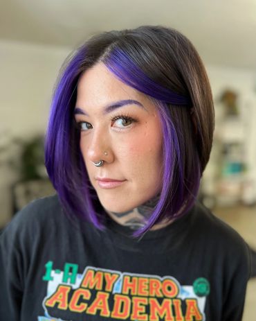 Young woman with purple-streaked bob haircut and septum piercing.