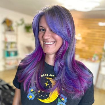Woman with vibrant purple and pink hair smiling indoors.