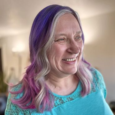 Smiling woman with gray hair dyed purple and pink tips.