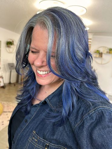 Woman with blue and silver hair smiling and looking down.