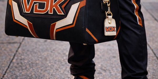 Stylish black and orange VDK leather duffle bag held by a person in matching outfit.