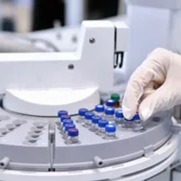 Gloved hand handling vials in a laboratory analyzer.
