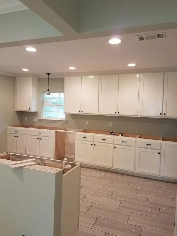 A kitchen with white cabinets being installed and no countertops yet.