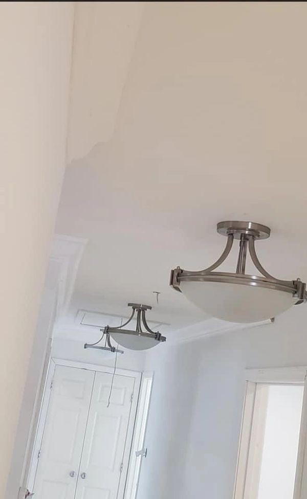Modern ceiling lights hang in a white hallway with a closed double door.