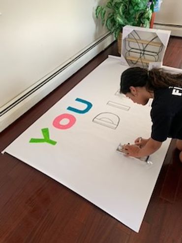 A person creating a large sign with colorful letters on a white board.