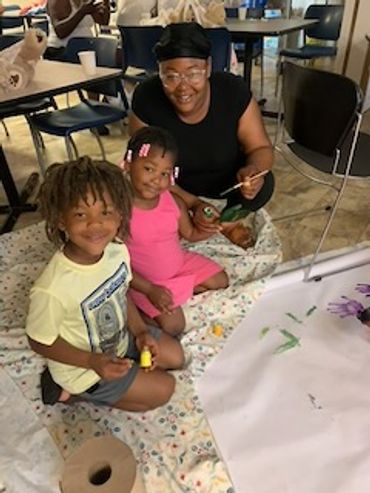 Three people joyfully painting together on a large canvas indoors.