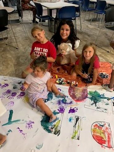 Children and a young woman enjoying a colorful painting activity on a large sheet.