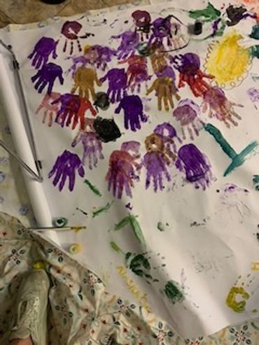 Colorful handprints in purple, red, and brown on white paper, surrounded by art supplies.
