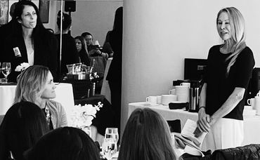 A woman speaks to an attentive group at a formal indoor event.