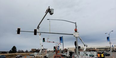 Workers use bucket trucks to install or repair traffic lights on a cloudy day.