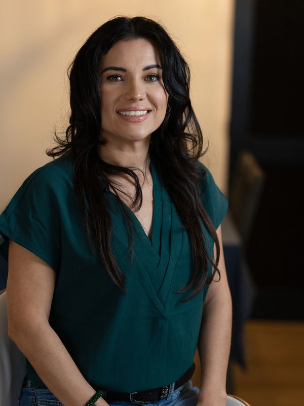 Smiling woman with long dark hair in a teal blouse.