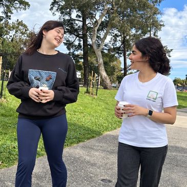 Little Light support worker and participant walking through a park with takeaway coffees.