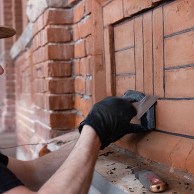 A person restoring a brick wall with a small tool.