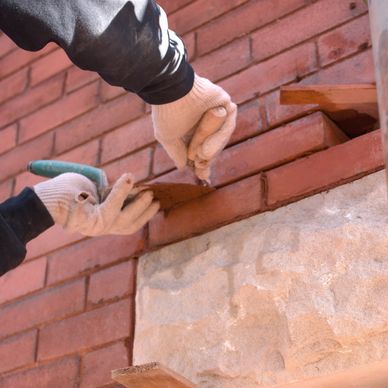 Hands in gloves laying red bricks on a wall with mortar.