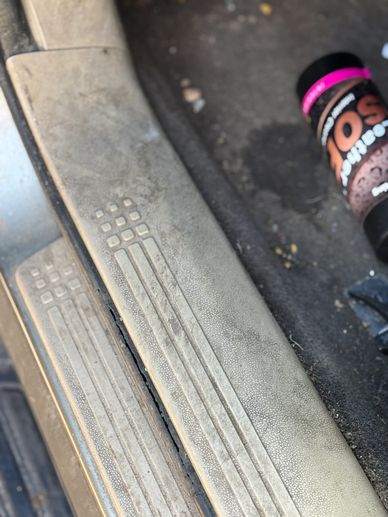 Dirty car door sill with a black bottle lying on the floor mat.