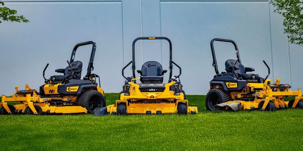 Three yellow Wright zero-turn lawn mowers parked on green grass.