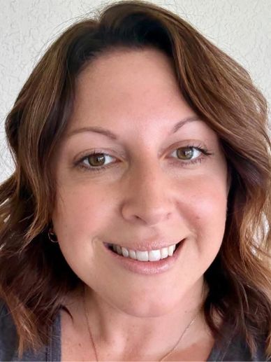 A smiling woman with wavy brown hair and hazel eyes.