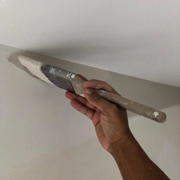 Painter with a painting brush creating a line between wall and ceiling. 