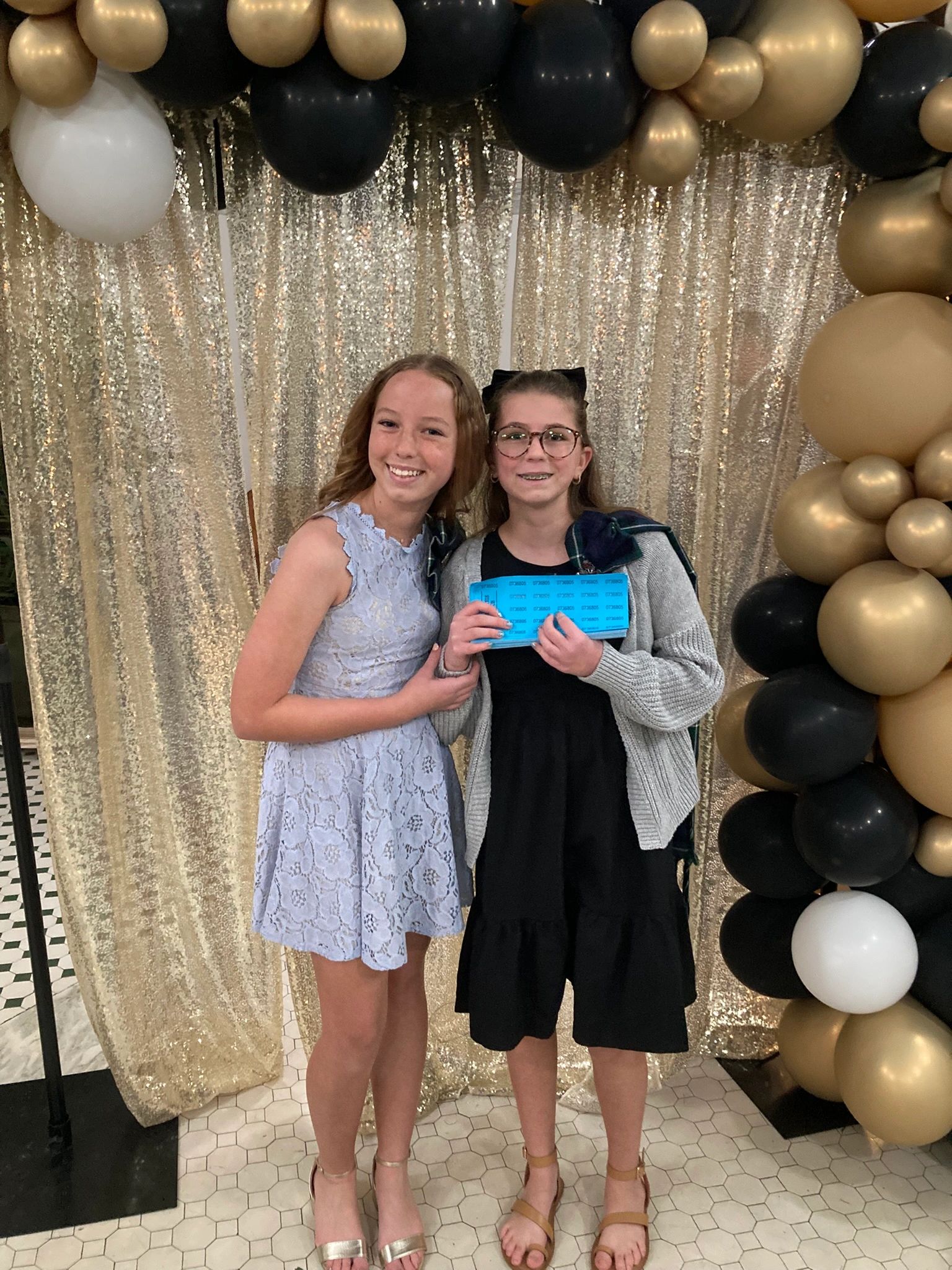 Two girls smiling at a party with gold and black balloons.
