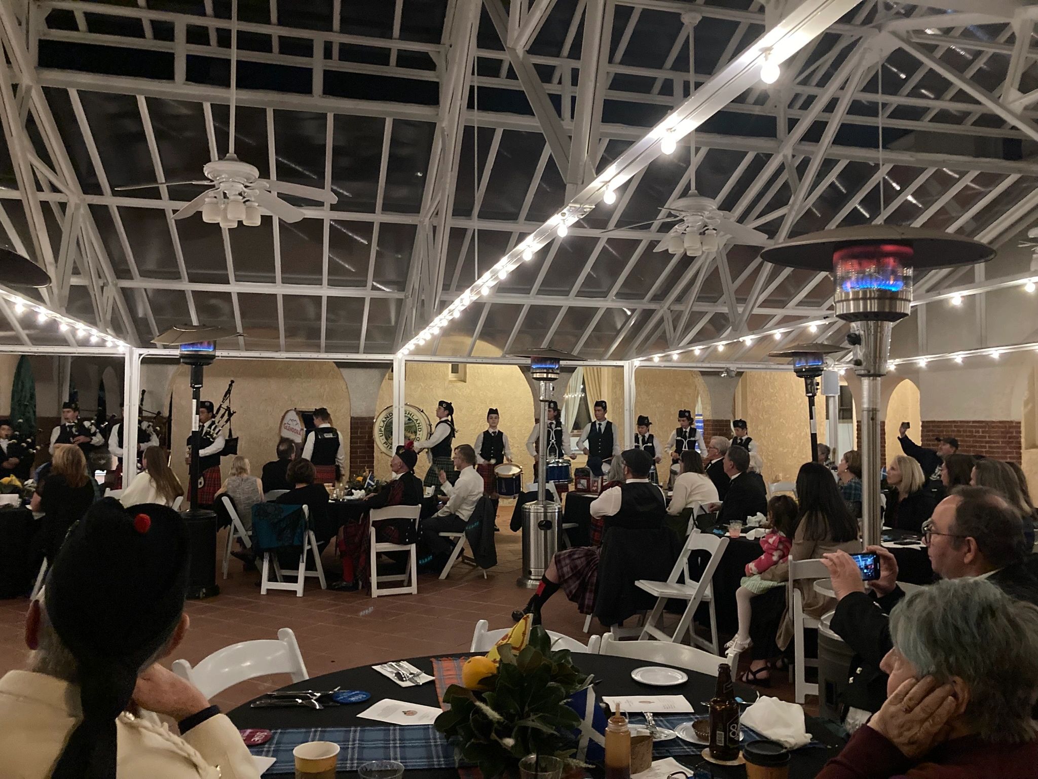 Indoor event with people in traditional Scottish attire and bagpipes.