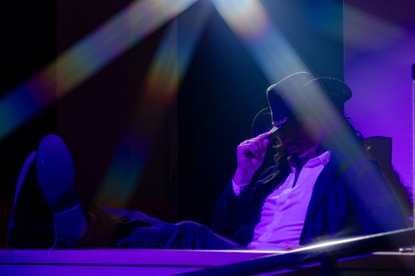 Man in a hat sitting with legs up, illuminated by colorful light beams.