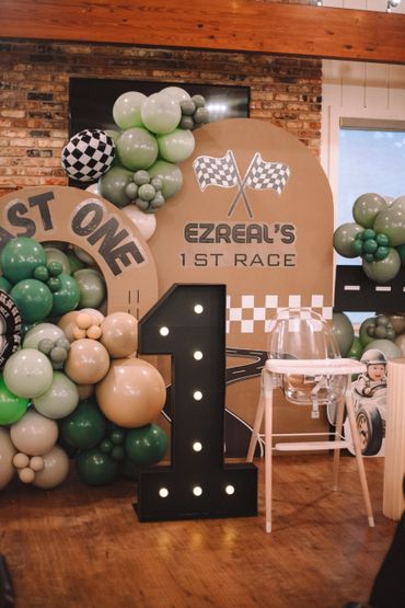 A first birthday racing-themed party setup with balloons and a large illuminated number one.