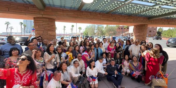 Large group of people posing under a shaded structure with flags.