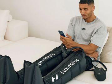 Man using a Normatec leg recovery device while checking his phone.