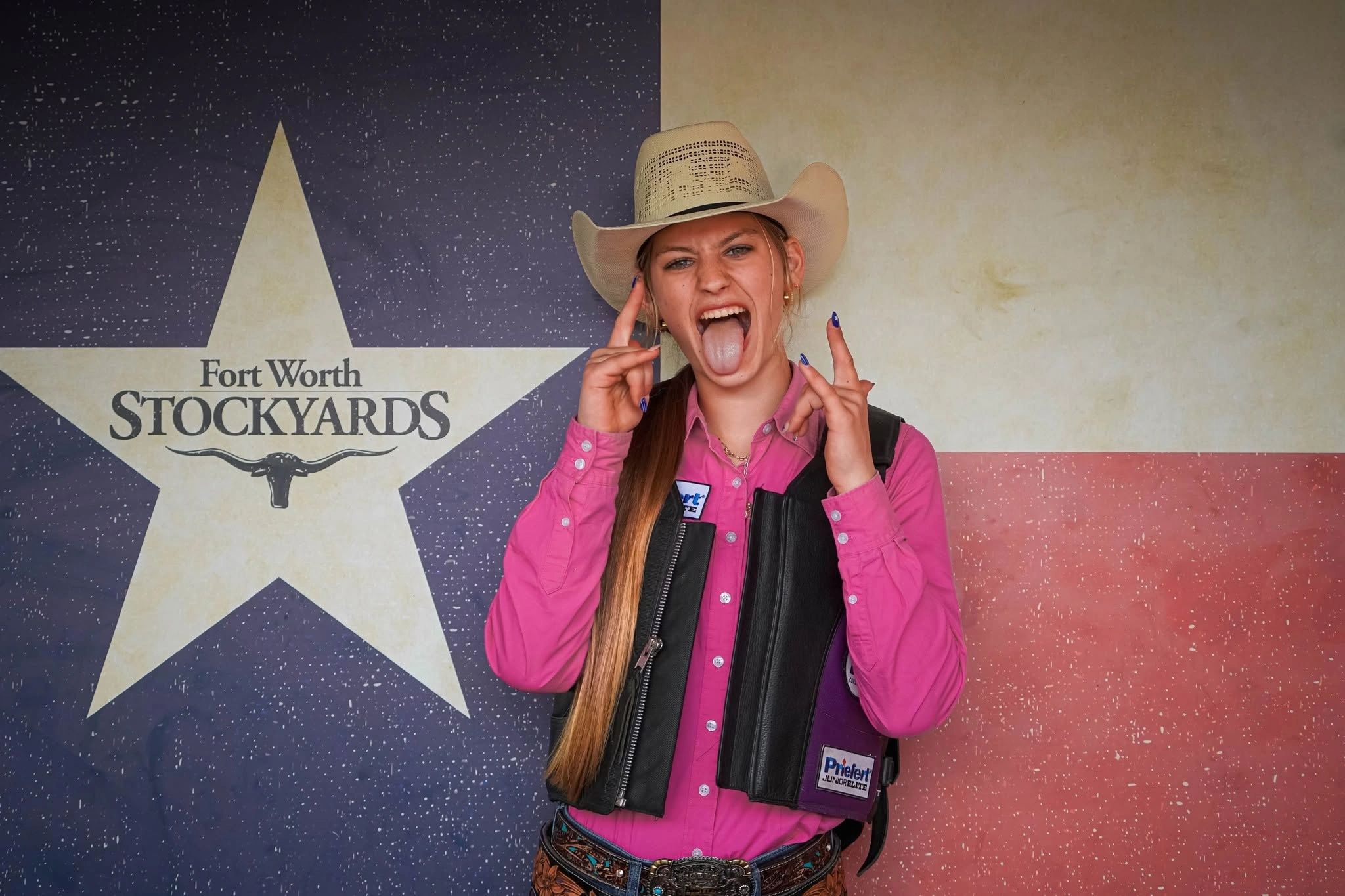Cowgirl making rock hand signs and sticking out her tongue at Fort Worth Stockyards.