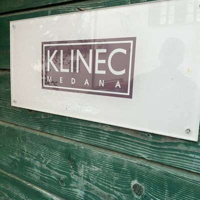 A white sign with the text 'KLINEC MEDANA' mounted on green wooden wall.