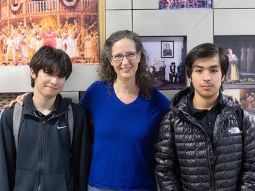 Three people posing indoors with framed pictures on the wall behind them.