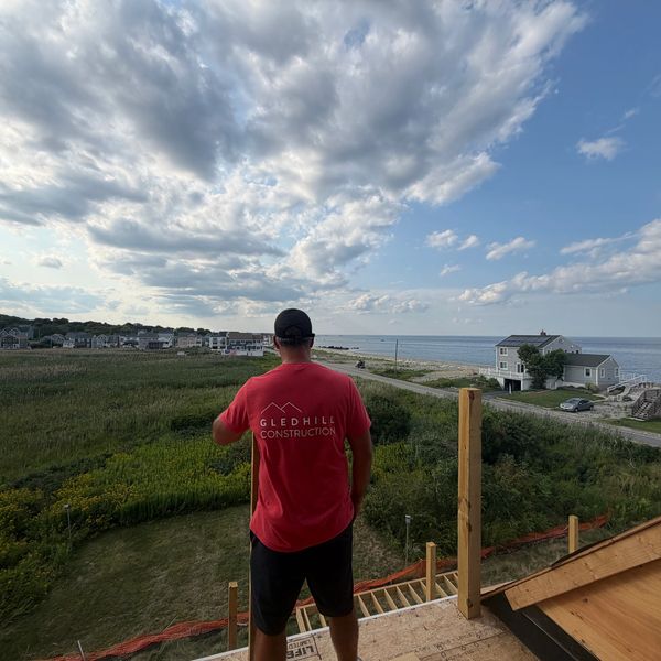 Man in red shirt overlooking coastal landscape.