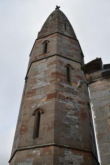 Tall stone tower with narrow arched windows and a pointed top.