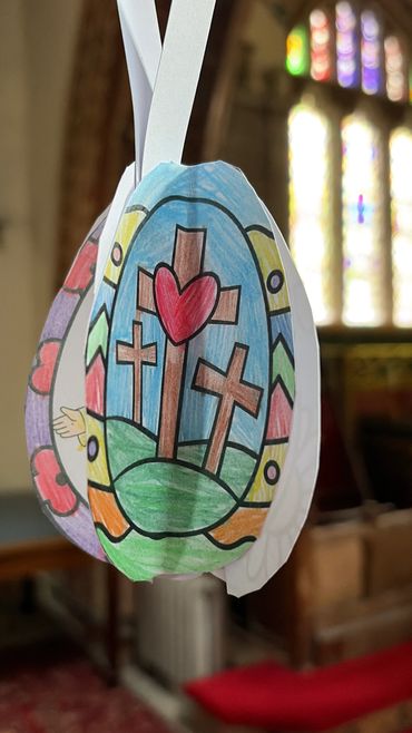Colored paper Easter decoration with three crosses and a heart hanging in a church.
