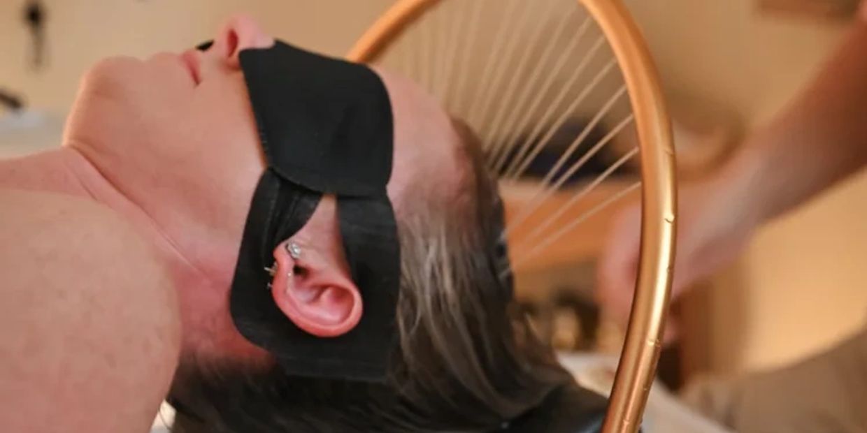 Person blindfolded with black cloth, head near a golden ring.