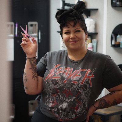 Smiling hairstylist holding pink scissors in a salon.