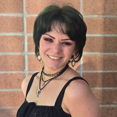 Young woman with dark hair smiling against a brick wall.