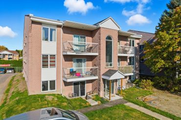Three-story apartment building with balconies under a bright blue sky.
