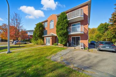 Three-story brick apartment building with balconies and surrounding greenery.