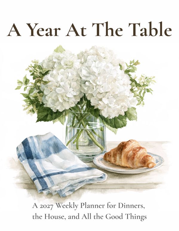 A Year At The Table 2027 weekly planner cover with flowers and a croissant.