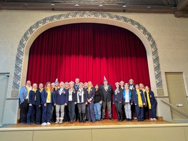 Group photo of people in formal attire standing on a stage with a red curtain.