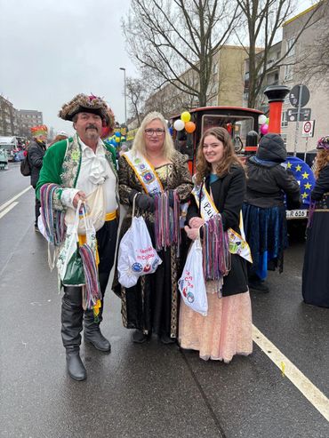Three people in festive costumes holding bags and beads at a street carnival.
