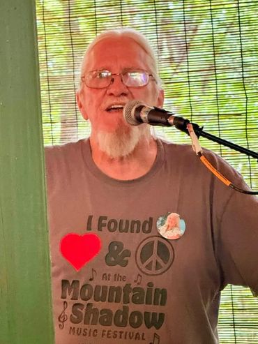 Elderly man singing into a microphone wearing a music festival shirt.